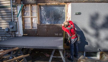 A person outside on a patio doing work on their house's insulation. A person outside on a patio doing work on their house's insulation.